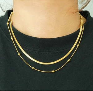 Details der goldenen doppellagigen Halskette mit flacher Schlangenkette und Perlenkette