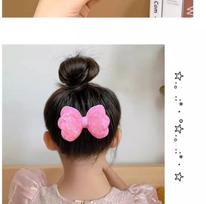 Close-up of a pink sequin bow hair clip worn on a girl's bun hairstyle