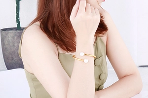 Detail of open gold cuff bracelet with white pearls worn on wrist for an elegant look
