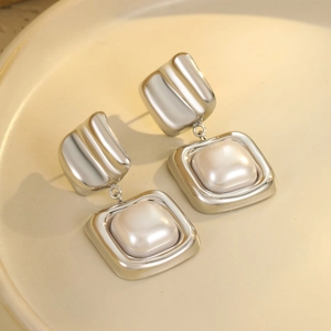 Close-up of geometric stainless steel earrings with baroque pearls on a ceramic tray