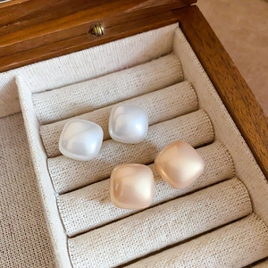 Close-up of square pearl earrings in cream and champagne colors on a wooden tray