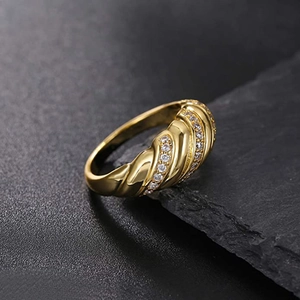 Gold twisted croissant ring with inlaid zircon rows displayed on a dark stone surface
