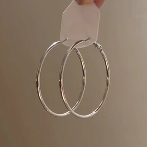 Detail shot of large silver hoop earrings held with card against a clean beige background