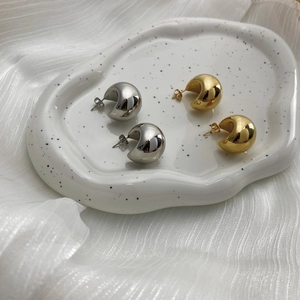 Macro detail of high-polish hollow gold and silver teardrop earrings on ceramic tray