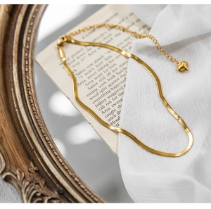 Close-up of gold snake chain necklace with heart pendant over vintage paper and silk fabric