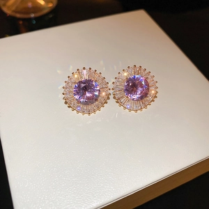 Macro shot of gold plated earrings featuring a purple zircon center with sunburst details