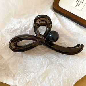 Détail d'une pince à cheveux nœud marron café avec perle noire sur fond blanc texturé