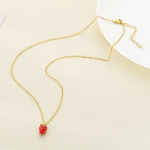 Close-up of a gold strawberry pendant necklace with red enamel and green leaf details