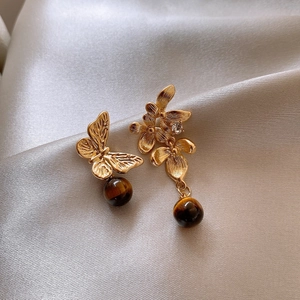 Asymmetric gold flower earrings with tiger eye stone beads on champagne satin background