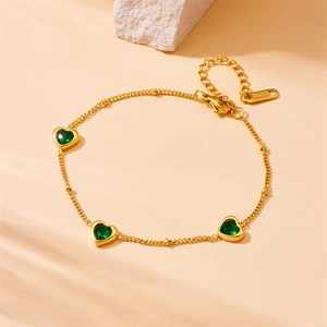 Gold stainless steel chain bracelet with three green heart-shaped gemstones on beige rock