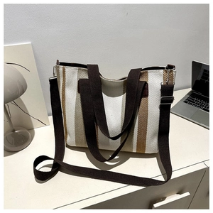 Detail of striped canvas tote bag showing metal hooks and adjustable strap on a desk