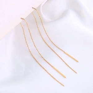 Close-up of golden tassel thread earrings with sleek metal bar detail on white silk