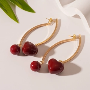 Detail of vintage gold curved earrings with heart-shaped dark red resin pendants