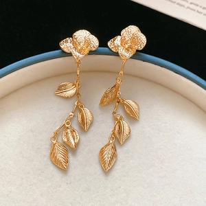 Detail of gold floral leaf tassel earrings showing textured veins on blue tray