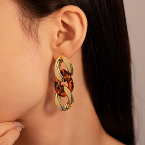 Close-up of leopard print acrylic and gold chain link drop earrings on a model