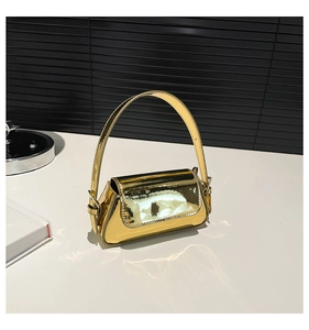 Detail view of the golden glossy patent leather material and flap closure of the handbag