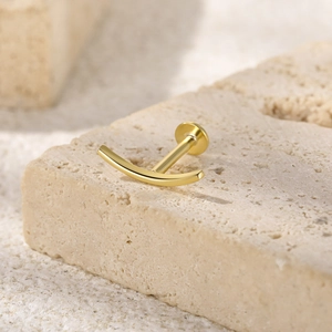 Macro shot of a golden curved labret stud earring on a natural textured stone background