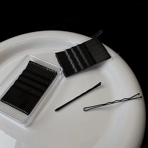 Macro view of matte black hair clips with wavy design in a clear plastic storage box