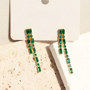 Elegant gold-plated drop earrings featuring emerald green zircons on a white display card