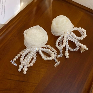 Detailed macro of white fabric rose earrings with pearl and crystal bow tassels
