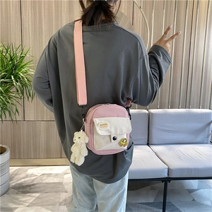 Sac bandoulière en toile rose et blanc avec peluche porté par un mannequin