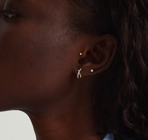 Close-up of elegant gold cross earrings and minimalist studs worn by a model