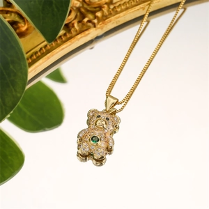 Detail of a gold teddy bear necklace with green gemstone and zircon pavé on a mirror