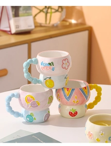 Close-up of assorted relief ceramic mugs featuring colorful cartoon patterns and beaded handles