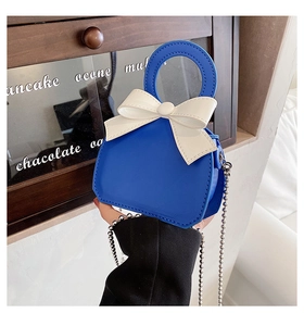 Close-up of a blue mini handbag with a white bow, metallic ball chain and glossy texture