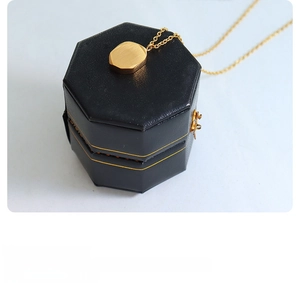 Macro detail of brushed gold octagonal pendant and fine cable chain on a black gift box