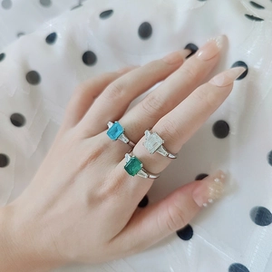 Macro shot of 2 carat rectangular moissanite rings in blue, green, and clear on model's hand