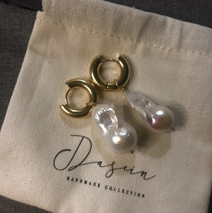 Elegant 18K gold hoop earrings featuring large Baroque pearls on a minimalist canvas pouch