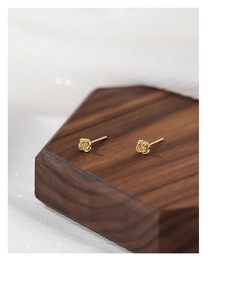 Macro shot of 3D rose gold flower earrings on a minimalist wooden hexagonal stand