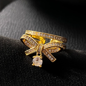 Macro shot of gold bow ring with sparkling clear stones and hanging round gemstone