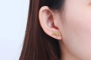 Close-up of golden abstract eagle head stud earrings worn by a model for a stylish look