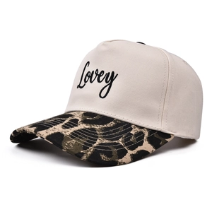 Detail of embroidered 'Lovey' text on five-panel cap with leopard print brim and light beige fabric