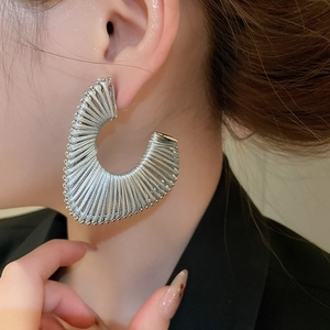 Detail of silver woven texture large C-shaped earrings worn by a model in close-up shot