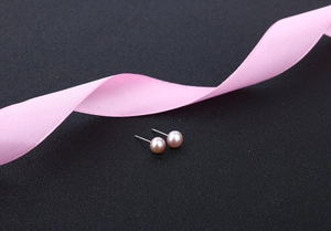 Close-up of elegant pink pearl earrings on black background with a silky ribbon detail