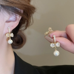 Boucles d'oreilles nœud dorées avec zircons et perles portées par une femme chic