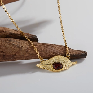 Close-up of leaf-shaped gold necklace with red garnet stone on dark wood background