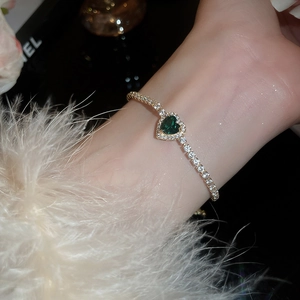 Macro shot of gold bracelet featuring heart-shaped emerald green gemstone and micro-pavé diamonds
