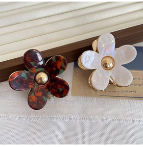 Detailed macro view of two floral acetate claw clips in tortoiseshell and pearly white finish