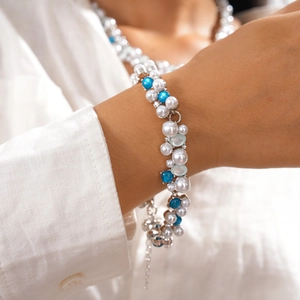 Detail view of pearl and blue bead bracelet set on a white textured linen background
