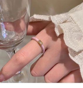 Close-up of square zircon ring with pink enamel drip on gold band worn on finger