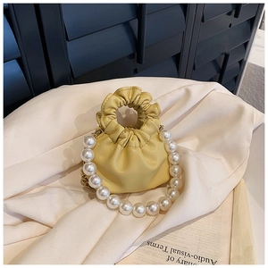 Detail of yellow pleated mini bucket bag with oversized pearl handle and soft leather texture