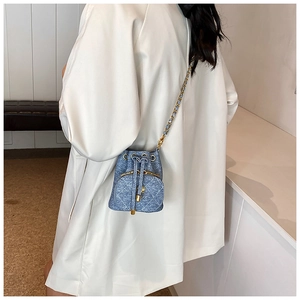 Side view of blue quilted denim bucket bag with gold chain strap on a model