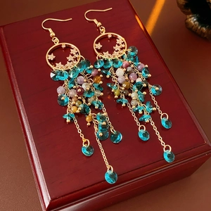 Close-up of vintage tassel earrings with teal crystal pendants on a wooden jewelry box