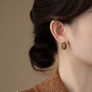 Close-up of gold oval stud earring with brown tiger eye stone and small pearl border