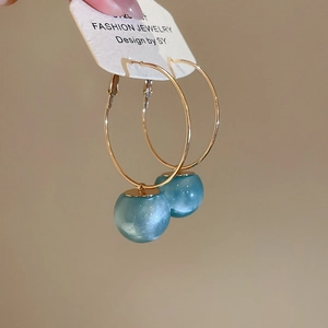 Detail of a gold circular hoop earring featuring a lustrous blue resin spherical pendant