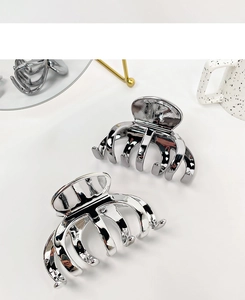 Detail of two glossy silver metal hair claws on a minimalist white background